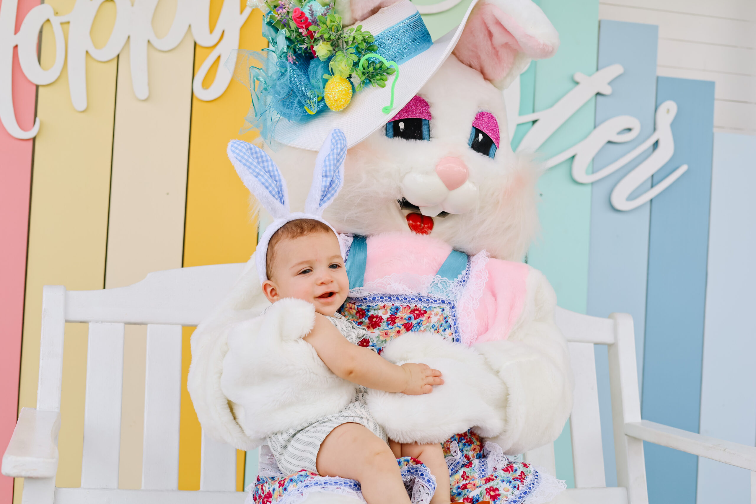 Picture of a baby wearing bunny ears taking a picture with the easter bunny.